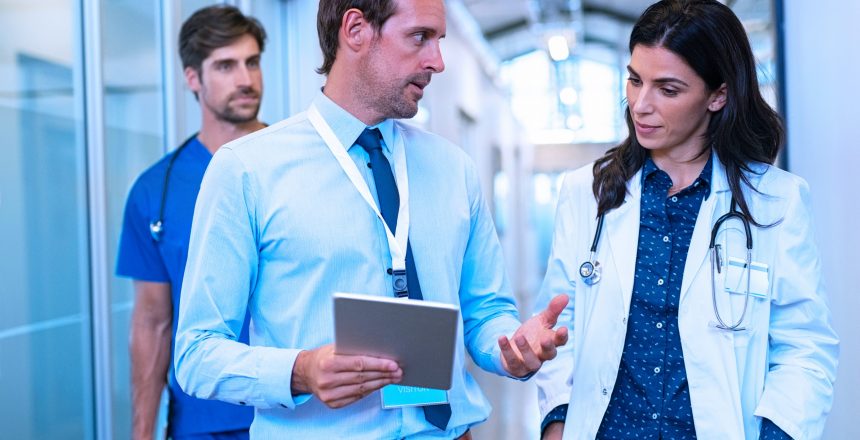 Man and woman doctor having a discussion in hospital hallway while holding digital tablet. Doctor discussing patient case status with his medical staff after operation. Pharmaceutical representative showing medical report.