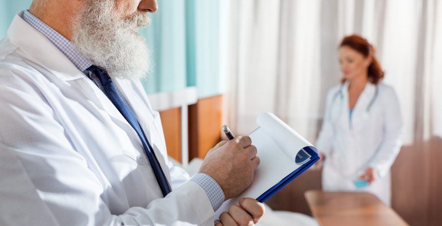 Senior male doctor making notes in clipboard in hospital